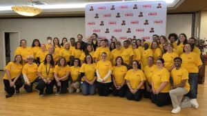 People wearing yellow The Caring Force shirts pose together in front of a The Caring Force backdrop.