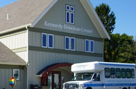 Photo of a large building with a white school bus in front of it.