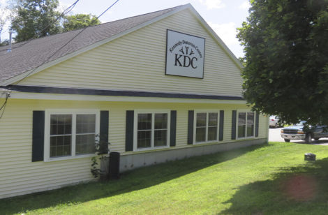 Sideview of a building with a sign on the top, and a tree to the right of the building.