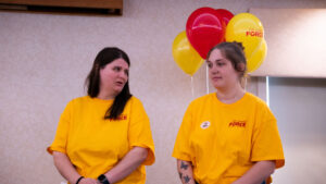 Two people wearing yellow The Caring Force shirts pose in front of a balloon display.
