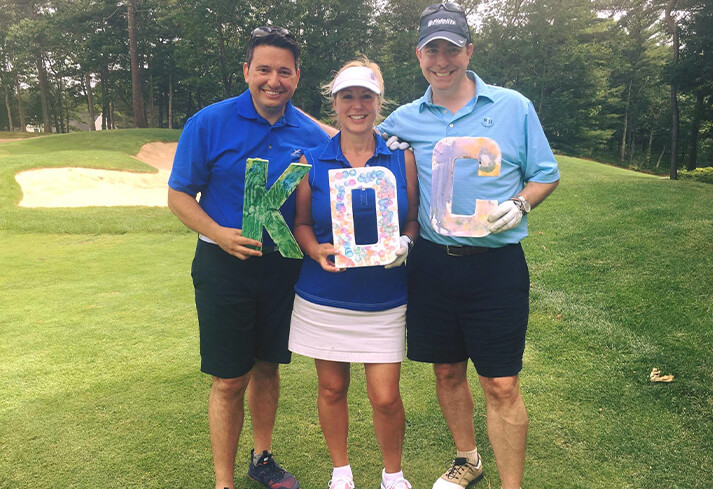 Three golfers posing with KDC letters on a putting green