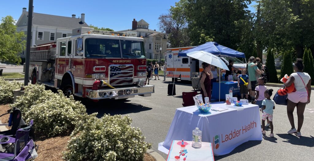 New Bedford first responder vehicles sit behind a resource fair table, surrounded by children and adults