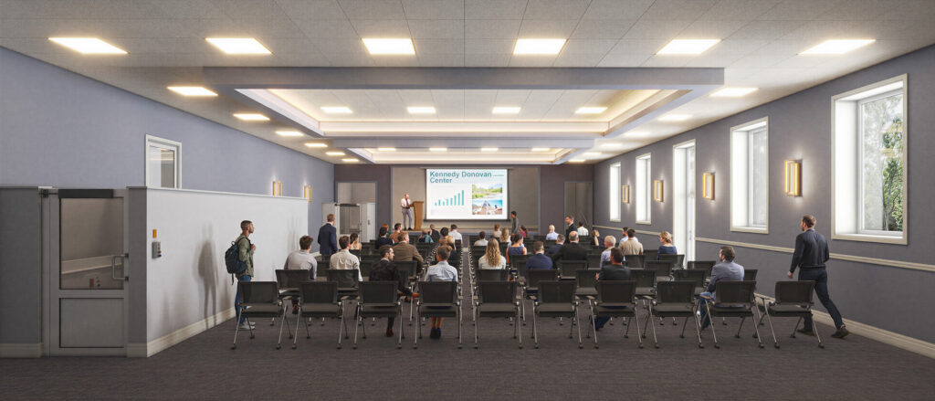 Digital rendering of how the center of impact can look, features a meeting being held with rows of chairs and people, and a speaker at the front of the room by a podium.