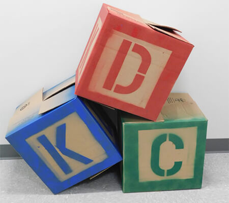 Cardboard bodes spraypainted to look like letter blocks stacked on top of each other to read KDC.