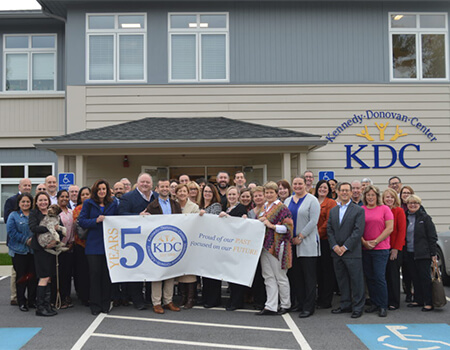 Dozens of people holding up a 50th anniversary banner in from of a building.