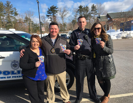 Police Officer's and citizens standing in front of a police car holding up autism patches.