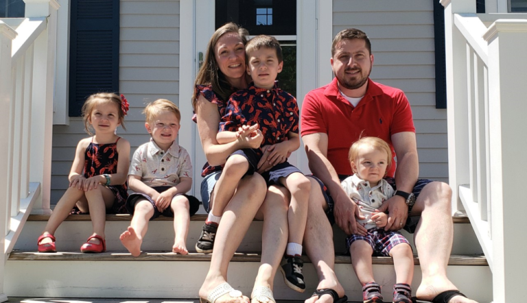 Parents with their four children sitting on their deck attached to a house.